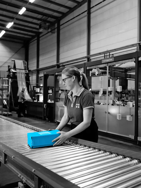 Monta-medewerker verwerkt een blauw pakket aan een rollenbaan in het magazijn